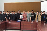 Caption: Hanafi, Ketua Cabang PSHT Sampang Jaket Hitam Saat Menyerahkan Berkas Pembaruan Legalitas Kepada Bambang, Kabid Politik Dalam Negeri Bakesbangpol Kabupaten Sampang