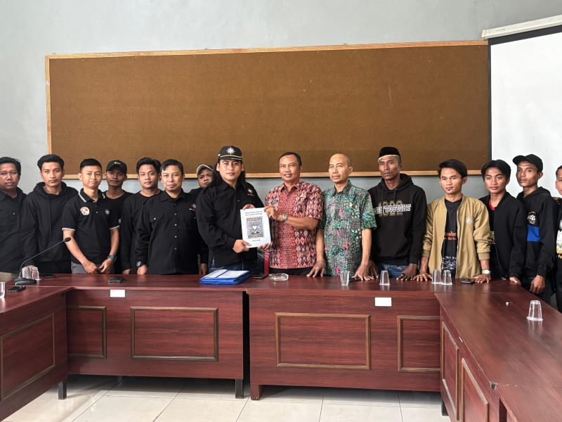 Caption: Hanafi, Ketua Cabang PSHT Sampang Jaket Hitam Saat Menyerahkan Berkas Pembaruan Legalitas Kepada Bambang, Kabid Politik Dalam Negeri Bakesbangpol Kabupaten Sampang